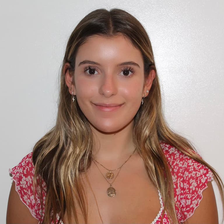 A person with long hair wearing a red floral top, smiling against a white background.