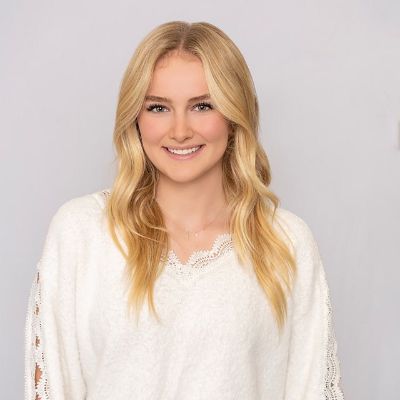 Person with long blonde hair, wearing a white sweater, smiling against a plain background.
