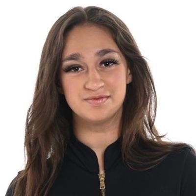 Young person with long brown hair wearing a black top, smiling at the camera.