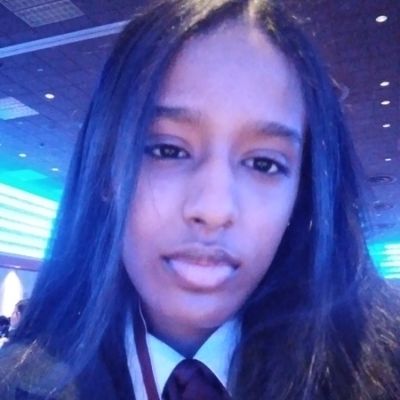 A person with long hair and a tie, indoors under blue and purple lighting.