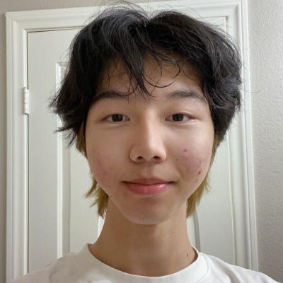 A person with dark hair smiling in front of a white door.