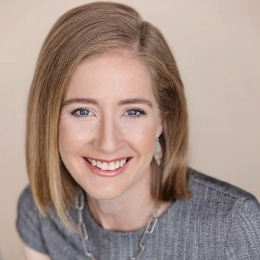Smiling person with shoulder-length hair, wearing a gray top and necklace, against a light background.