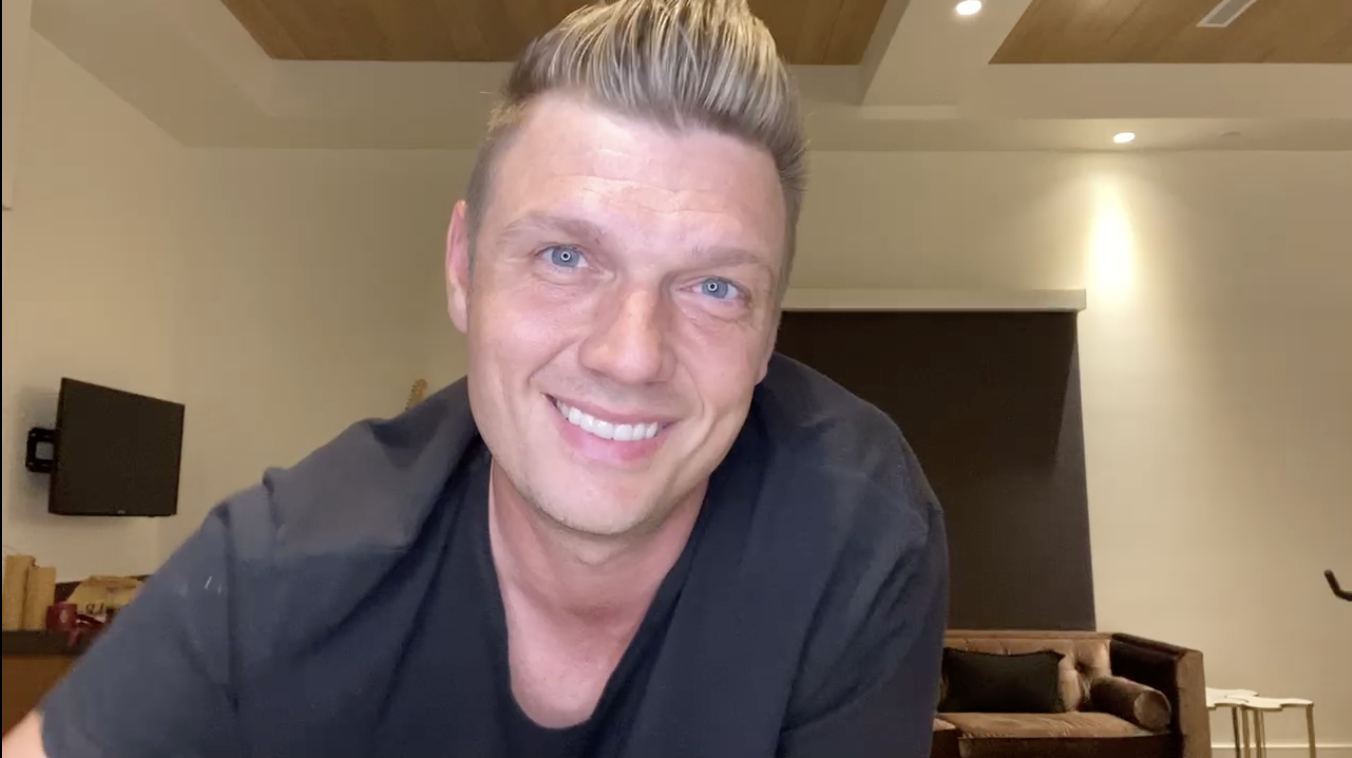 Man in a black shirt smiling at the camera in a modern living room setting.