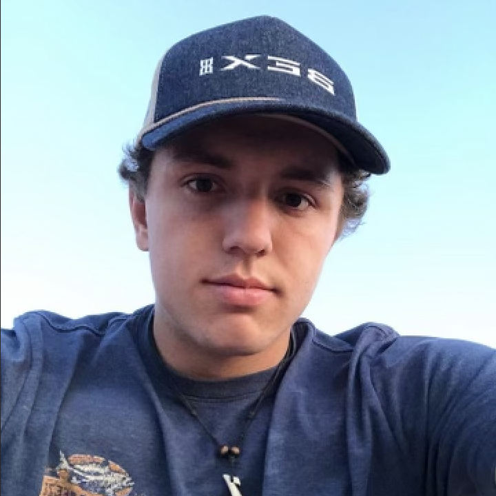 Young person in a blue cap and shirt looks into the camera against a clear sky backdrop.