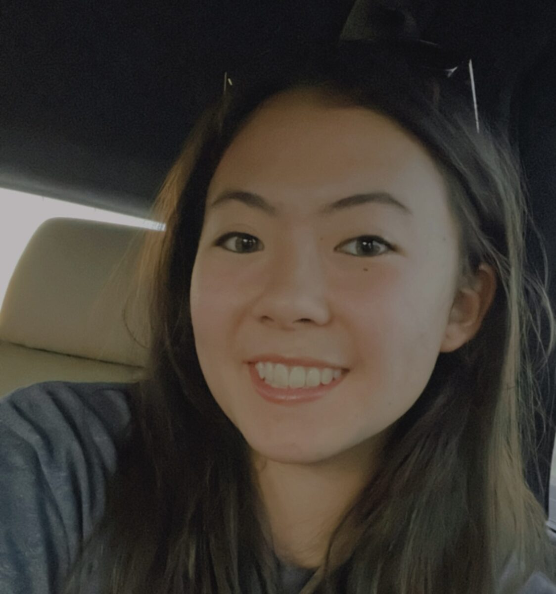 Young woman with long hair smiling while sitting in a car seat.