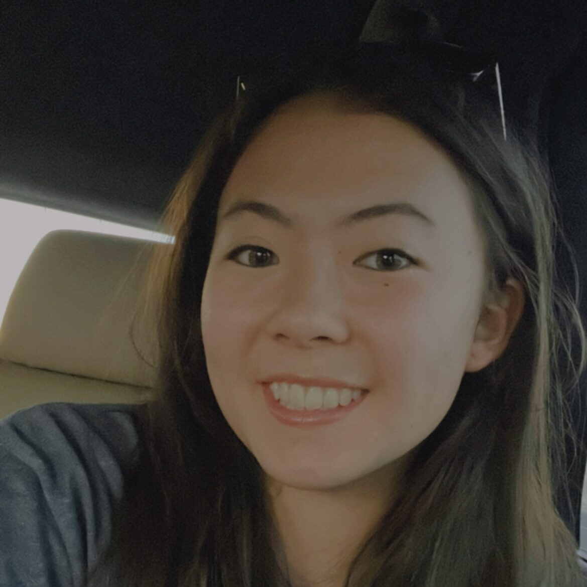 Young woman with long hair smiling while sitting in a car seat.