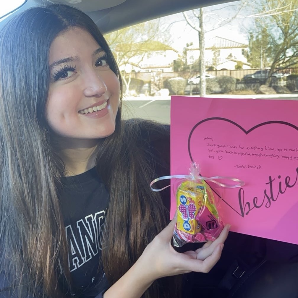 Smiling woman holds a pink card and a candy gift bag inside a car.