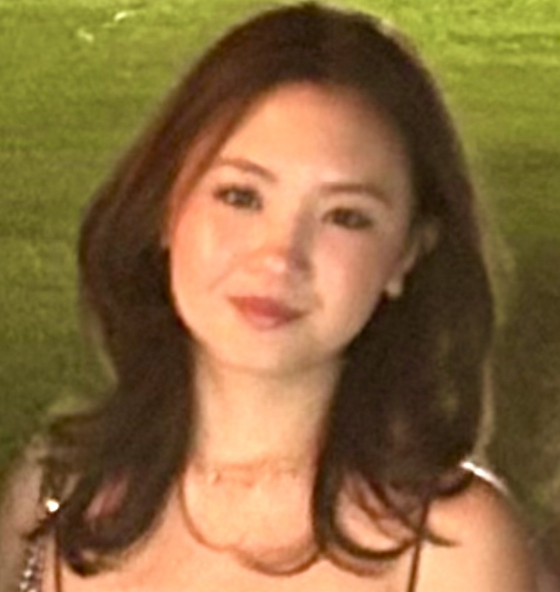 A person with shoulder-length hair smiles softly, standing outdoors.