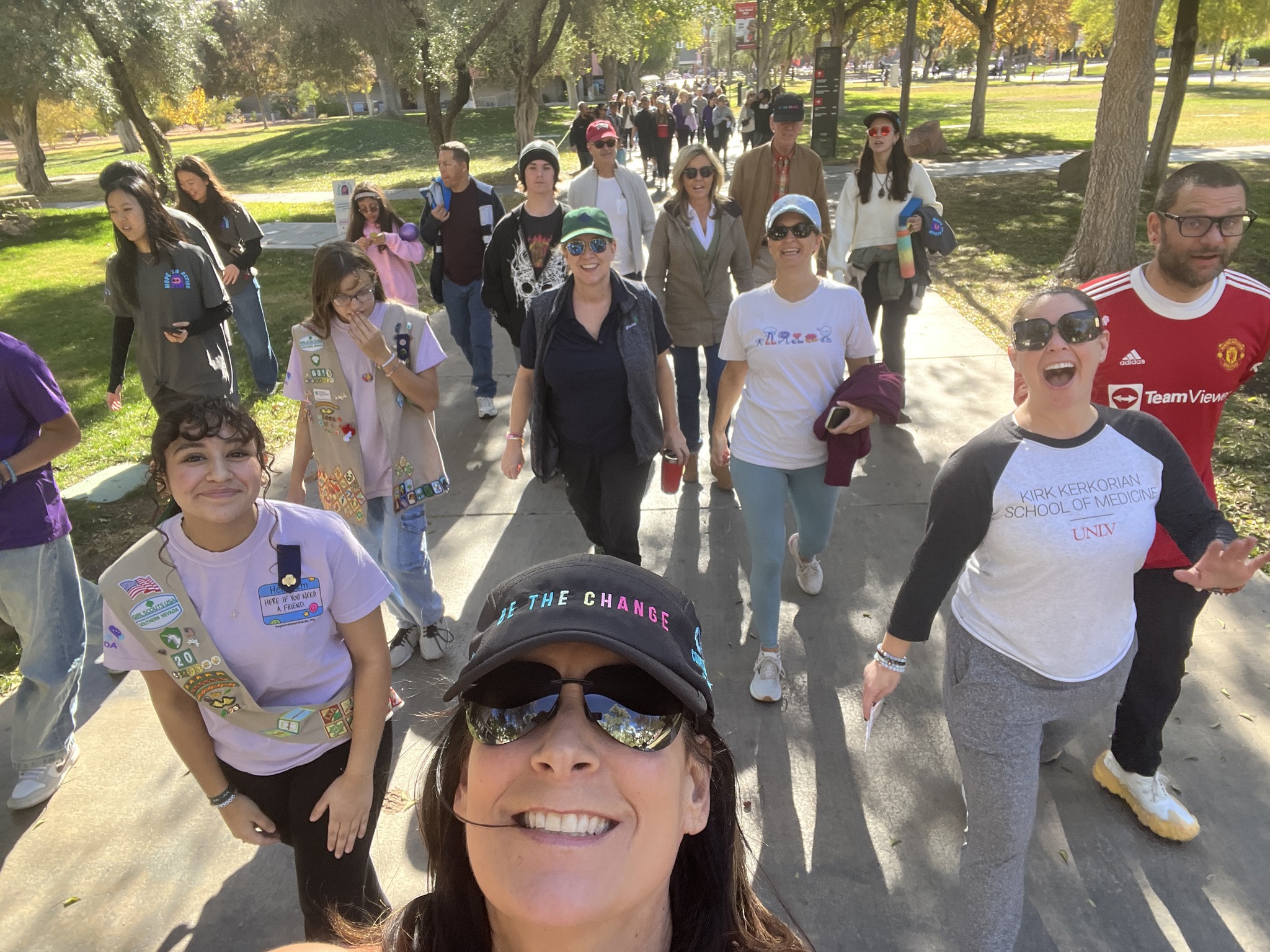 A diverse group of people smiling and walking together outdoors on a sunny day in a park.